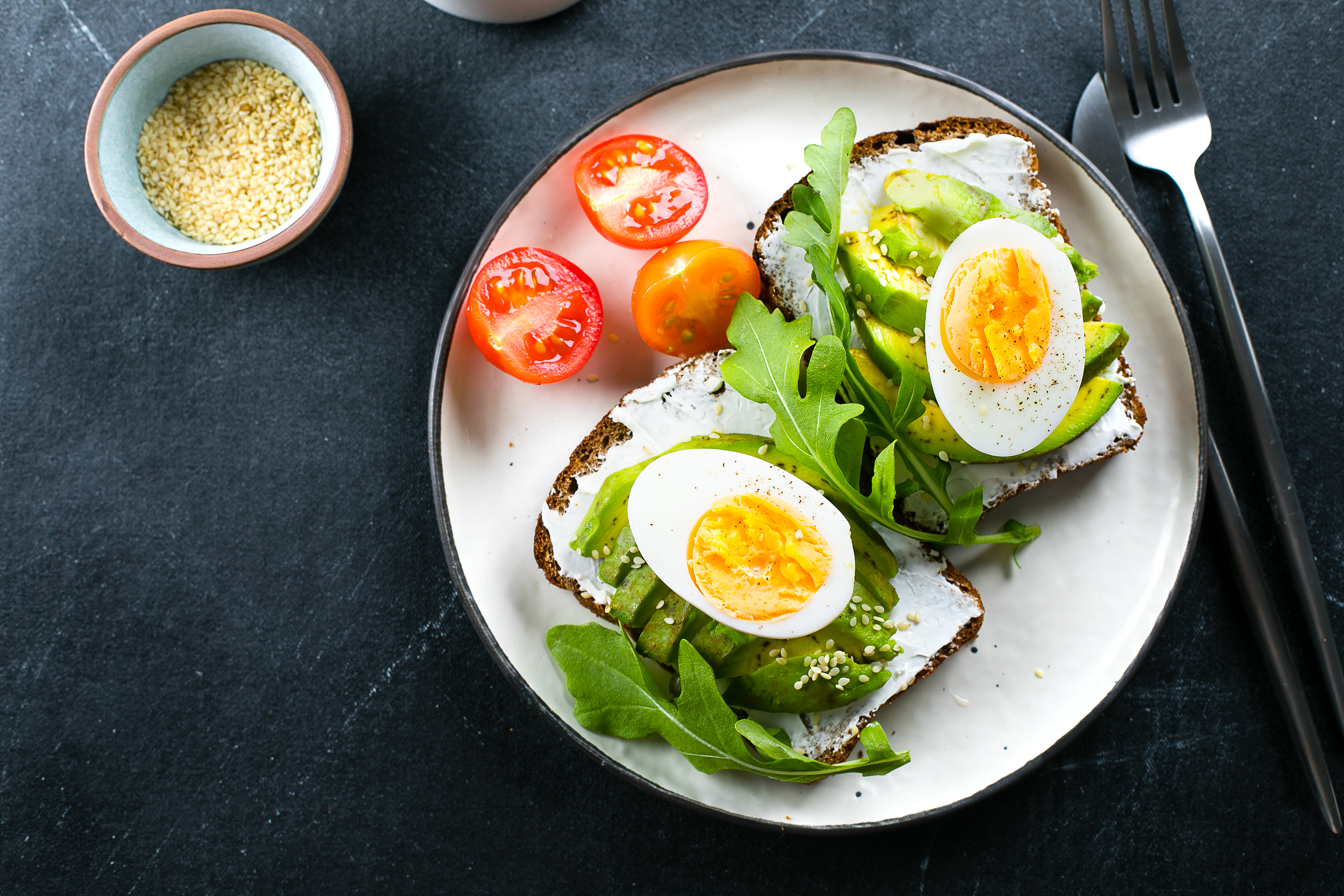 Avocado toasts with cottage cheese, eggs and arugula on darl table background. Healthy breakfast, snack. Top view