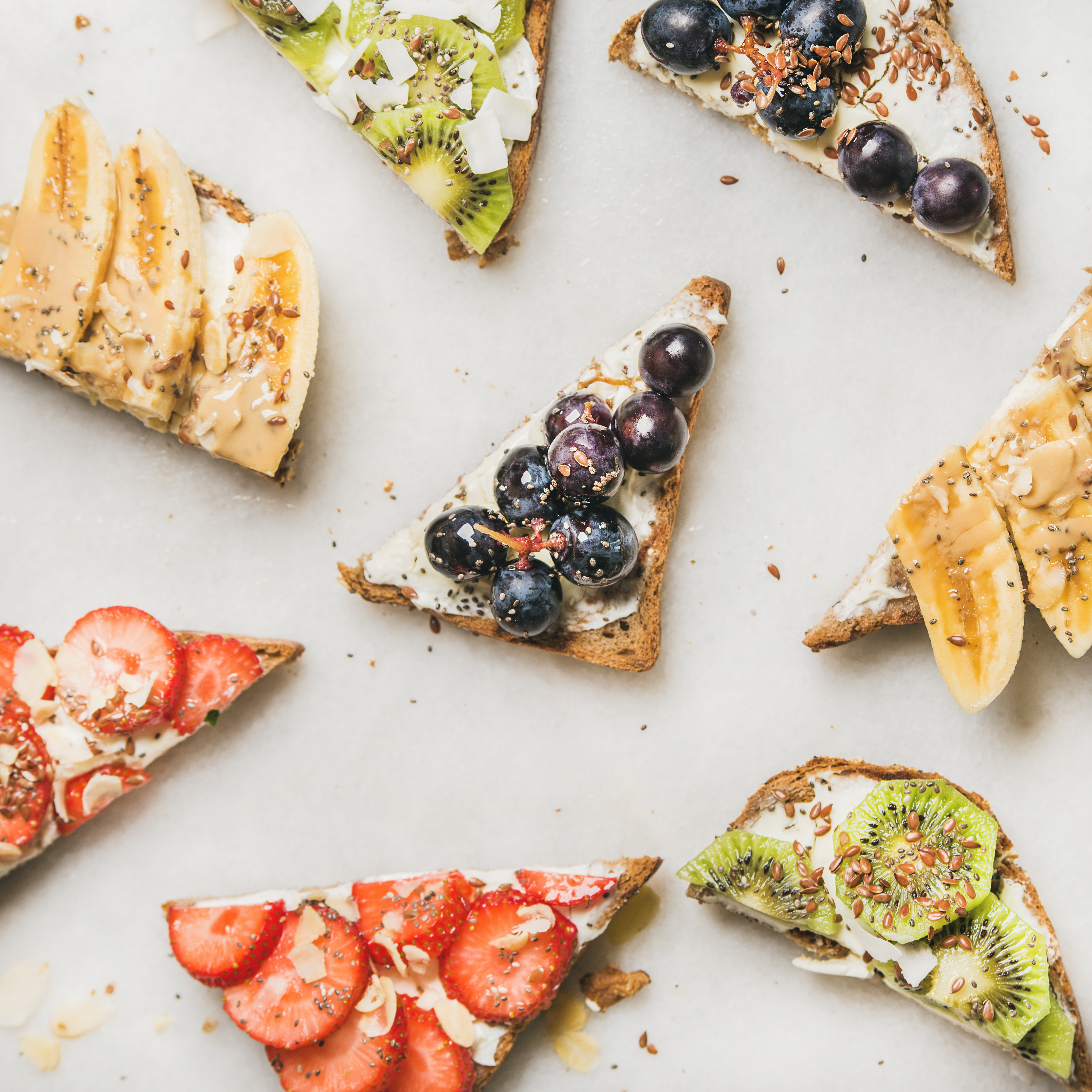 Healthy breakfast toast pieces. Wholegrain bread slices with cream cheese, various fruit, seeds and nuts. Top view, grey marble background, square crop. Clean eating, vegetarian, dieting concept