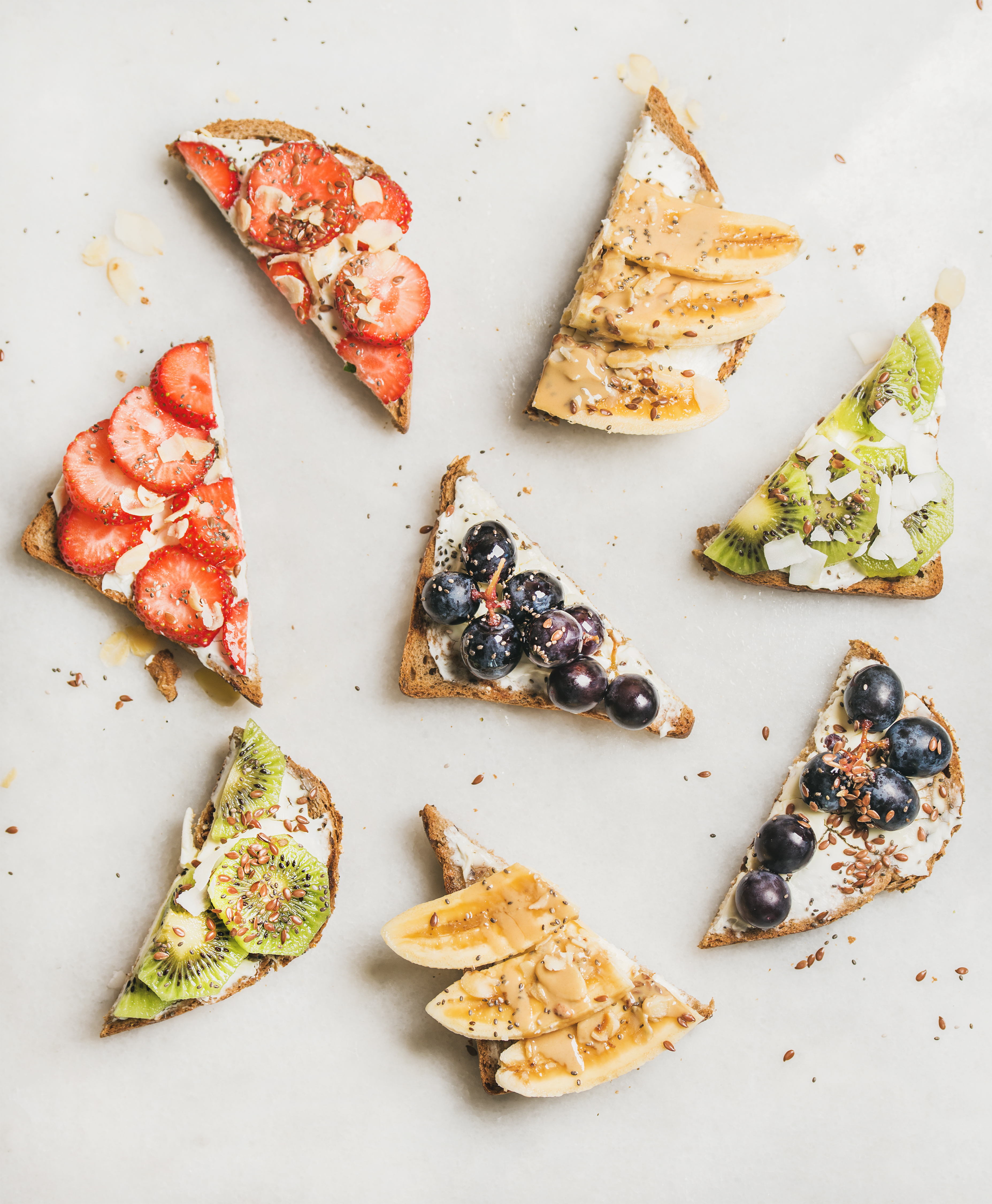 Healthy breakfast toasts cut in pieces. Wholegrain bread slices with cream cheese, various fruit, seeds and nuts. Top view, grey marble background. Clean eating, vegetarian, dieting concept