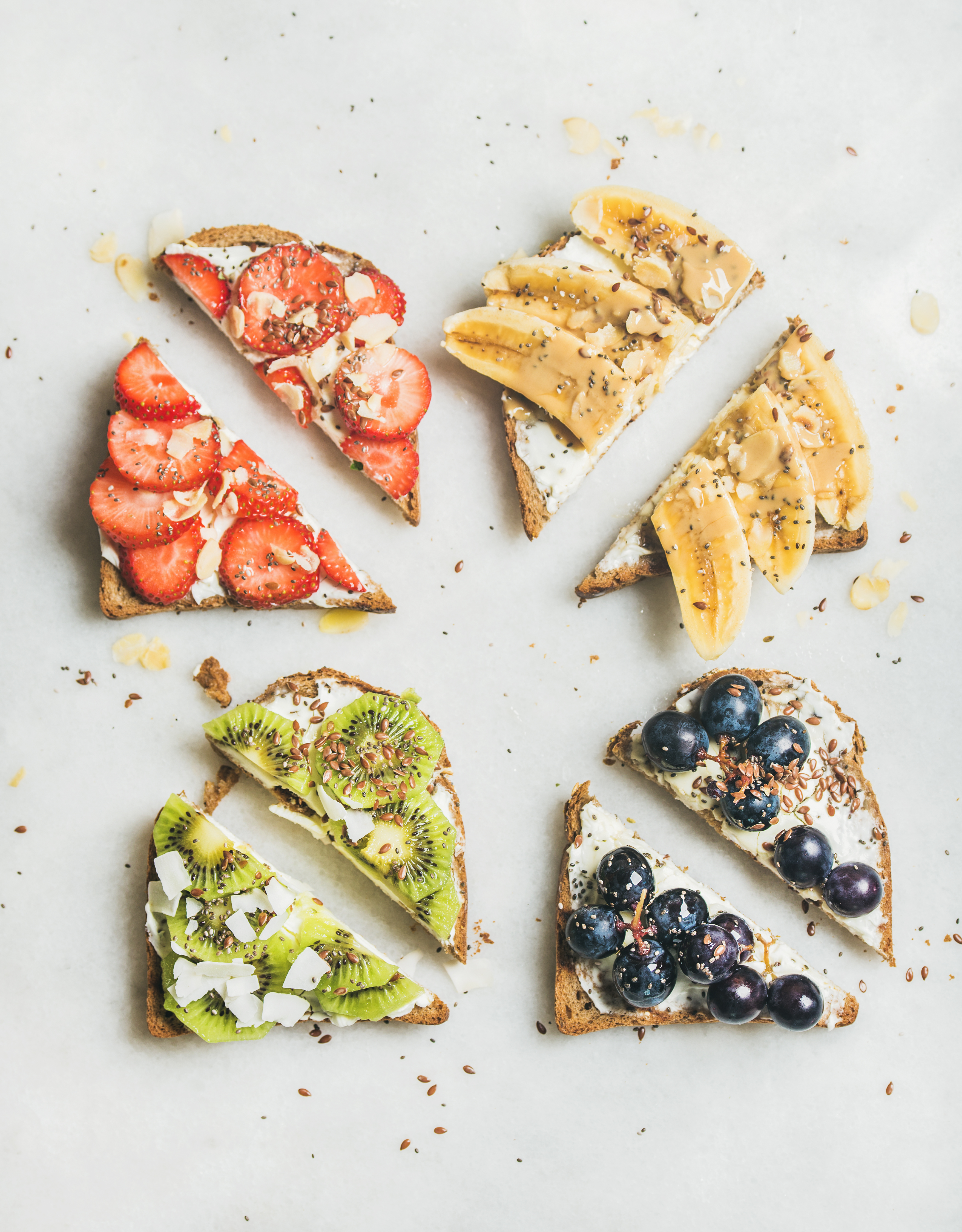 Healthy breakfast wholegrain toasts with cream cheese, various fruit, seeds and nuts. Top view, grey marble background. Clean eating, vegetarian, dieting, healthy lifestyle concept