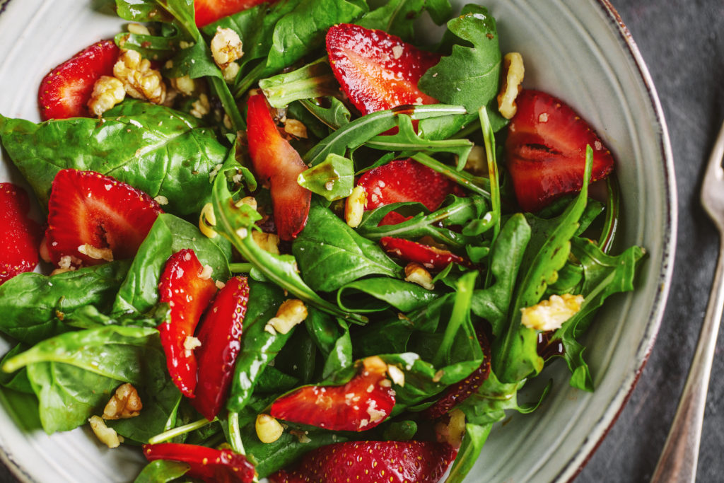 Tasty appetizing freshmade summer salad with arugula, strawberry and nuts served in bowl. Closeup