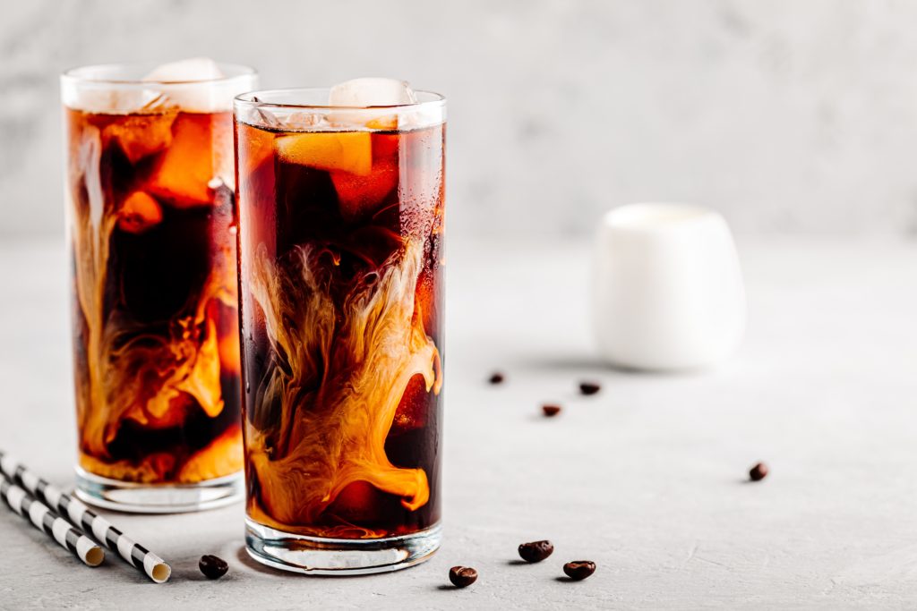 Coconut chai iced coffee with ice cubes in tall glasses on gray stone background
